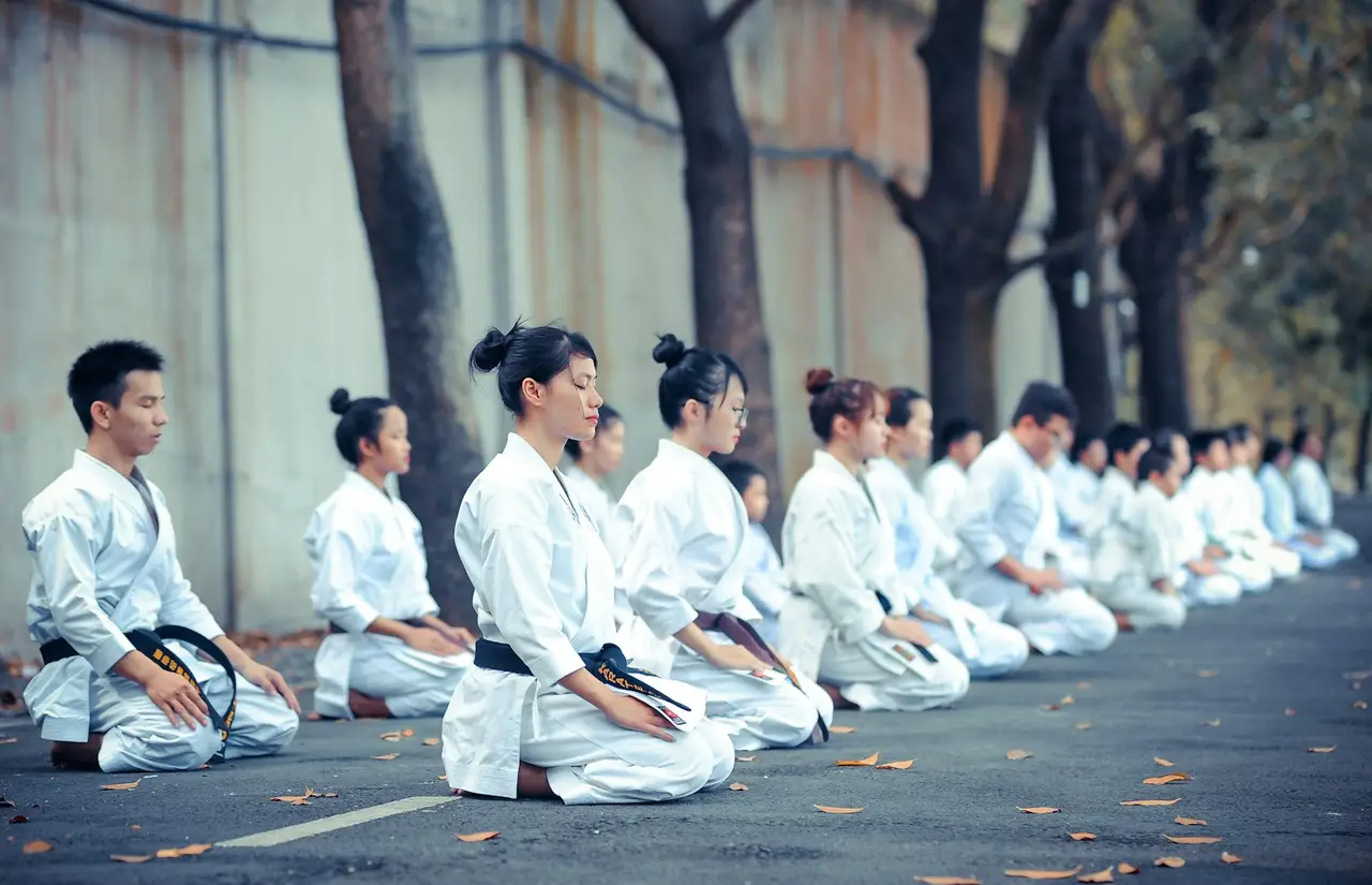 Karateka knien in weißen Anzügen aufgereiht zur Meditation.