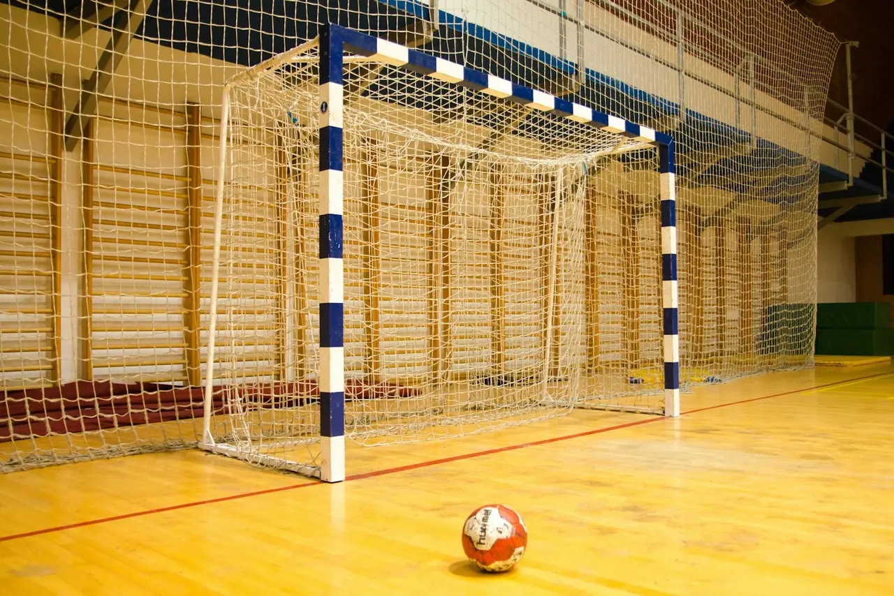 Ein Handball liegt vor einem Tor in einer Sporthalle.