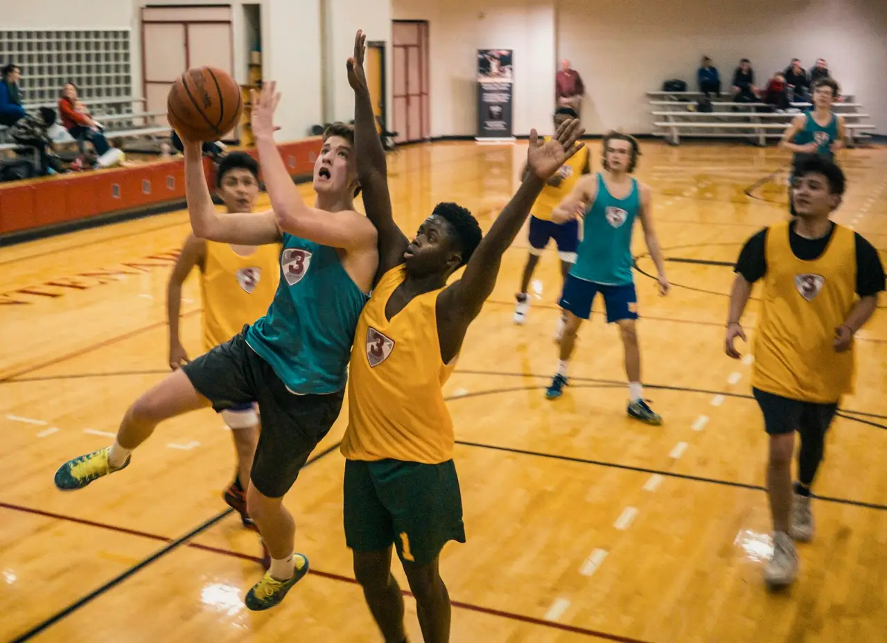 Jugendliche spielen in einer Halle Basketball.
