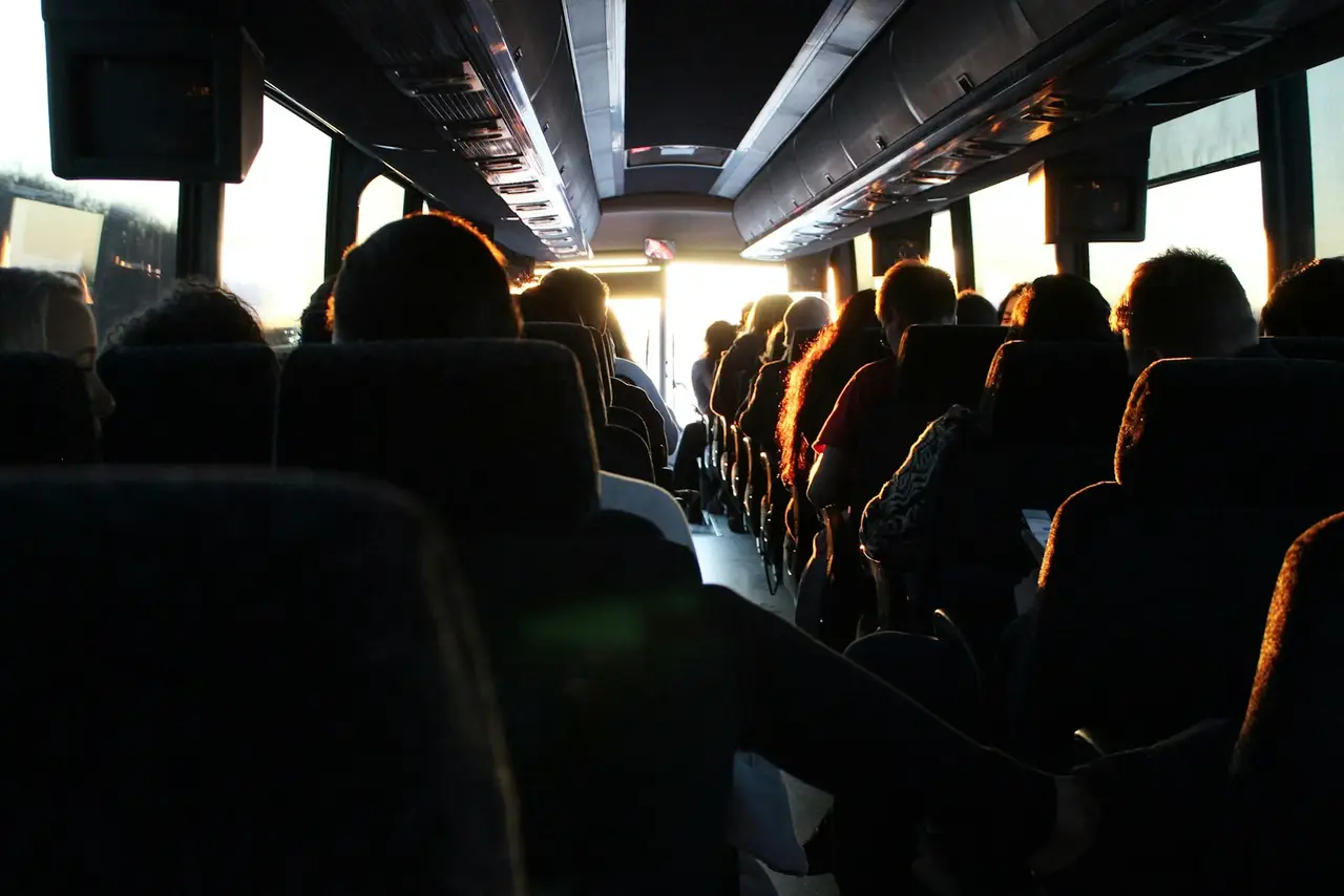Reisende sitzen in einem Bus, durch die Scheiben fällt Gegenlicht.