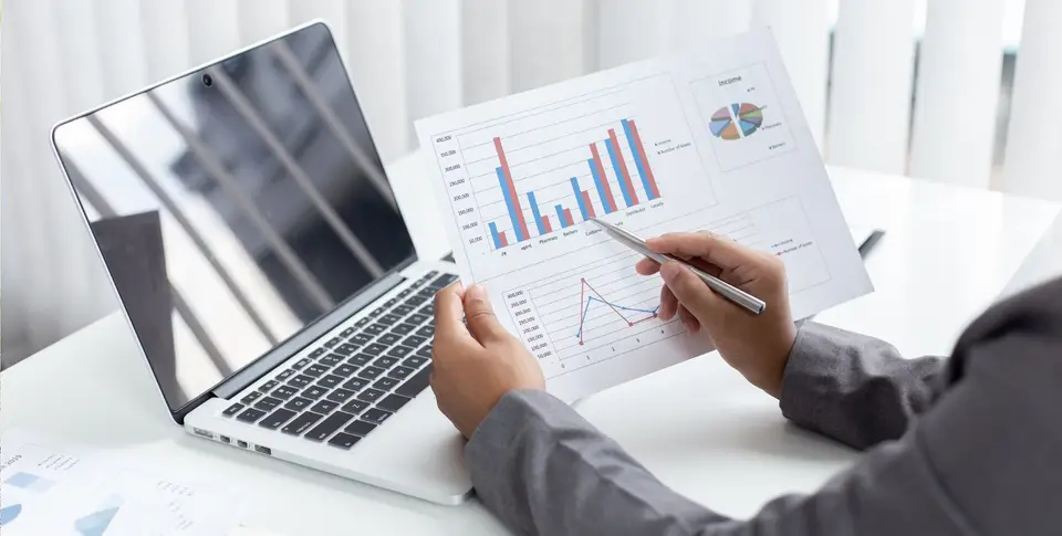 Eine Person prüft Diagramme und Finanzunterlagen am Laptop.