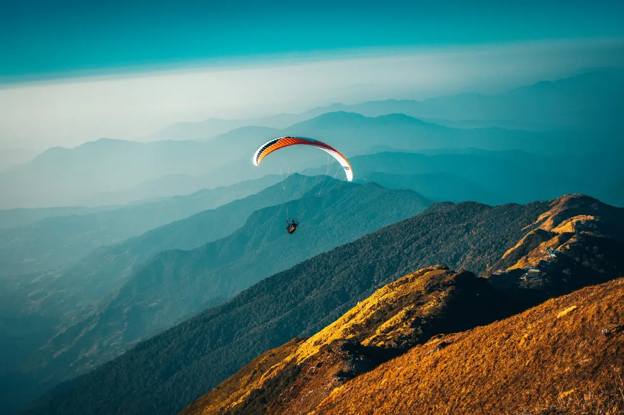 Eine Person fliegt mit einem Gleitschirm über eine Berglandschaft.