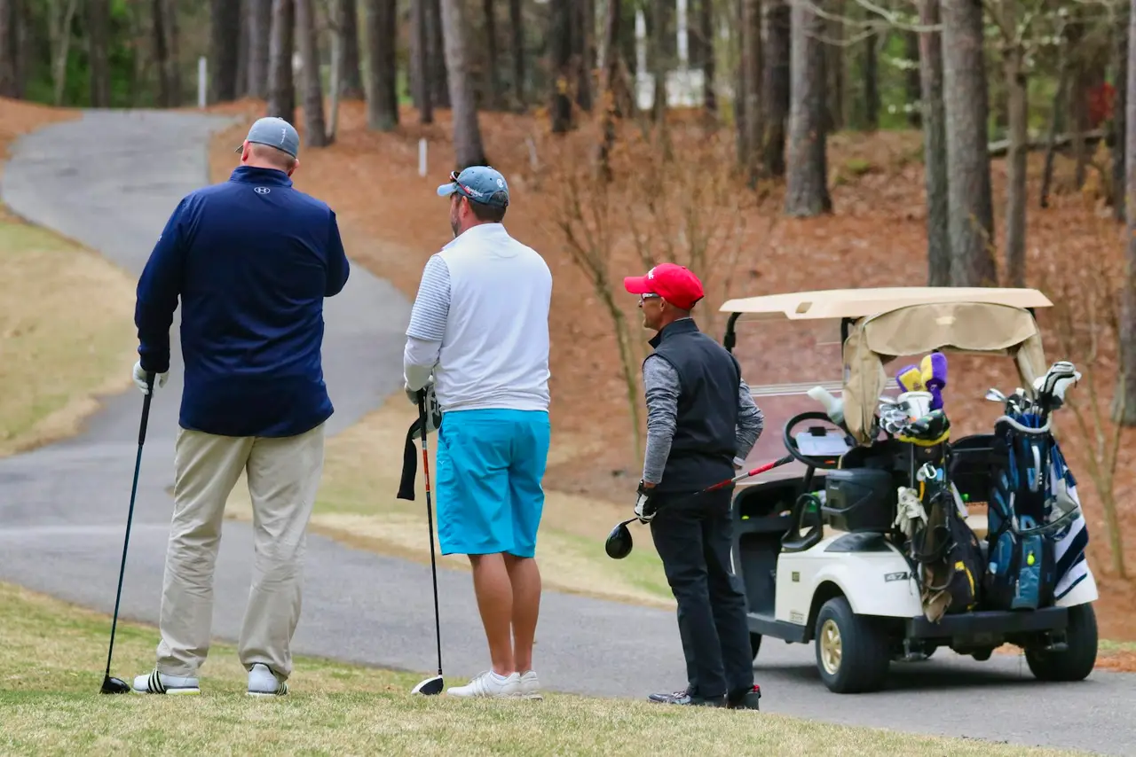 Drei Golfer stehen neben einem Golfcart und unterhalten sich.