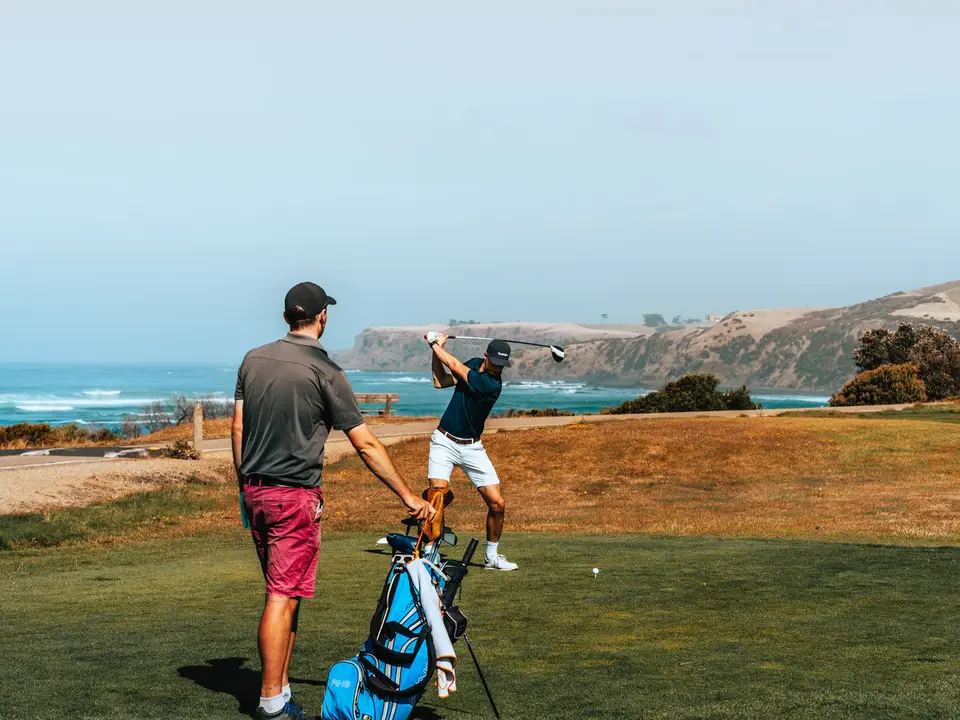 Ein Golfer beobachtet den Abschlag eines anderen Spielers an der Küste.