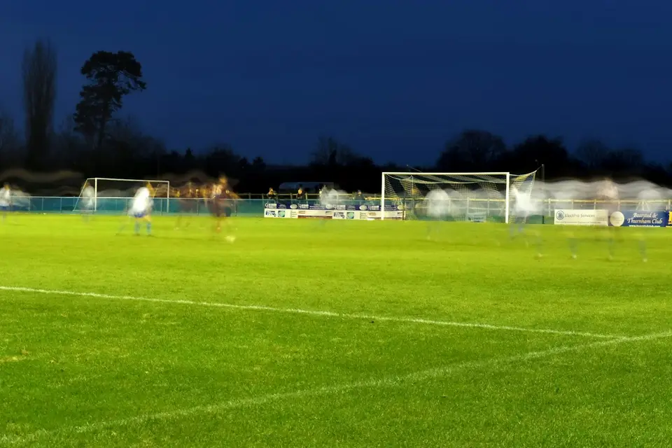 Spieler trainieren abends unter Flutlicht auf einem Rasenplatz.