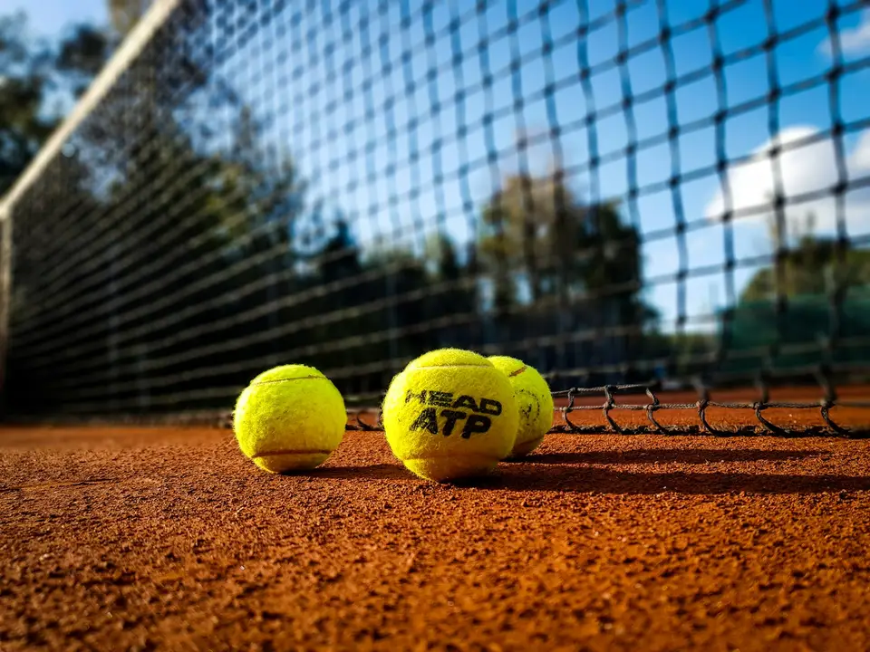 Tennisbälle liegen vor dem Netz auf einem Sandplatz.