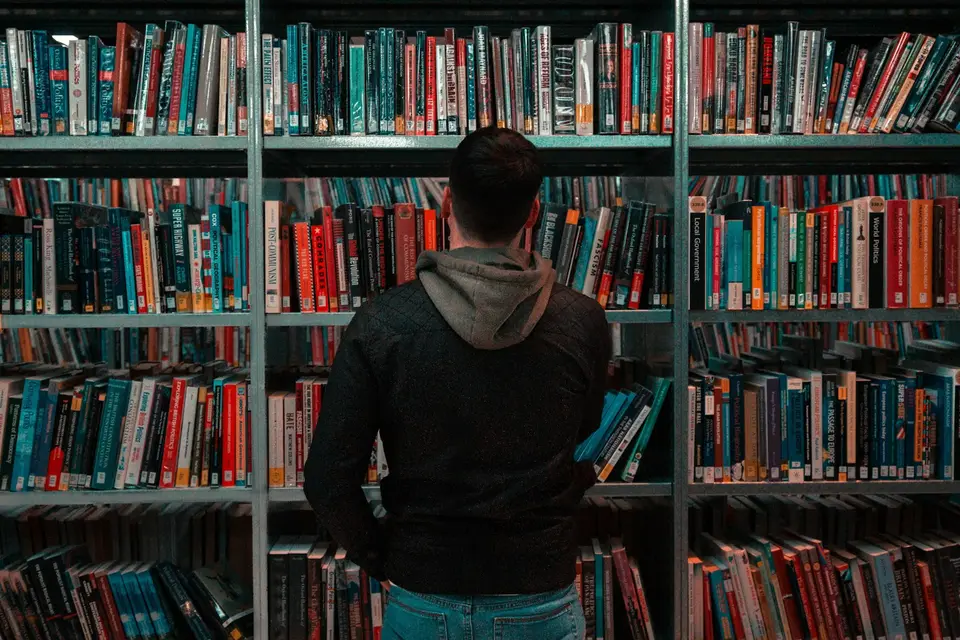 Ein Mann steht in einer Bibliothek vor Bücherregalen.