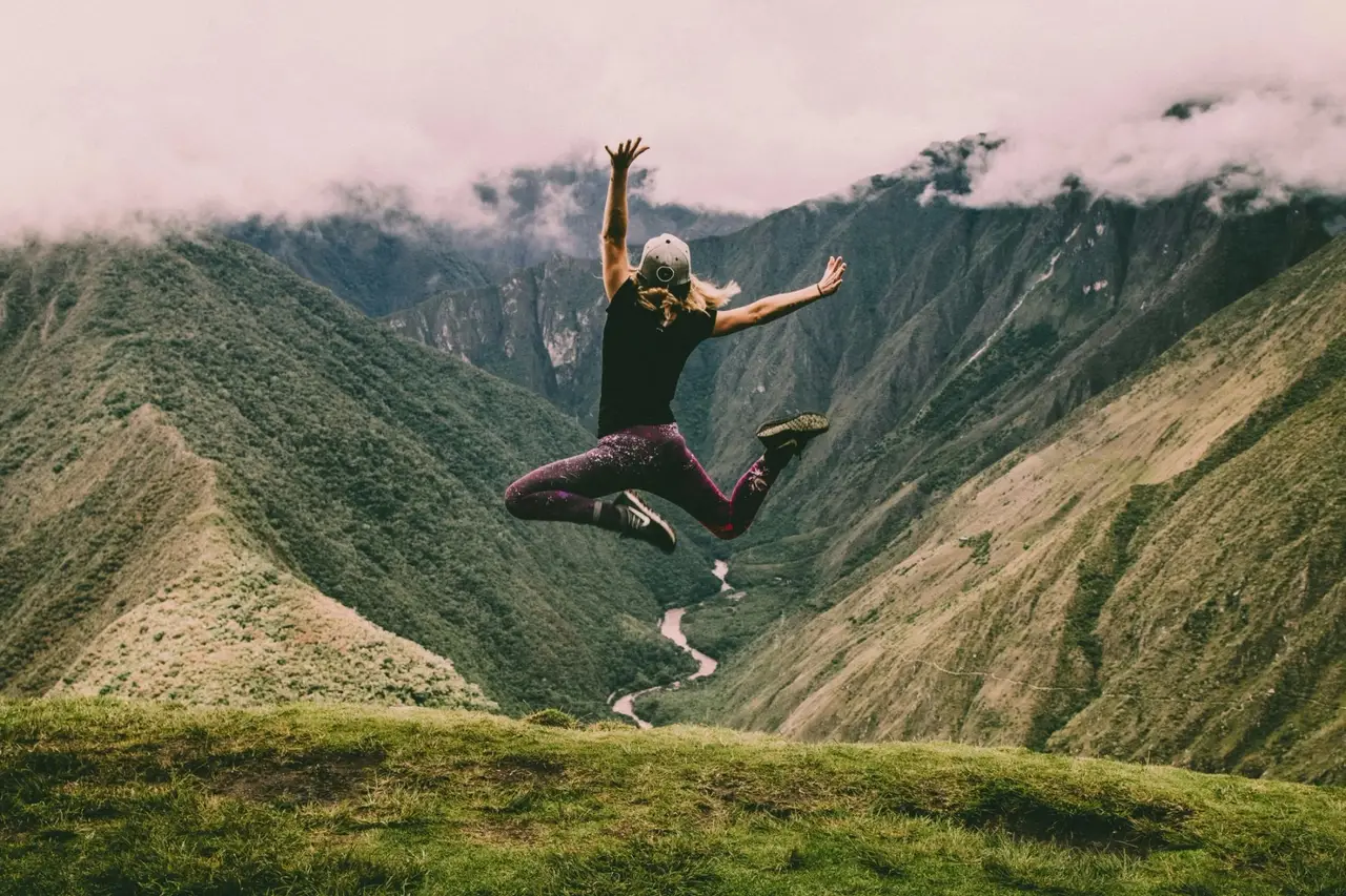 Junge Frau springt in die Luft vor einer Bergkulisse