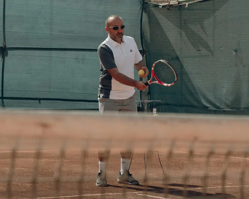 Ein Tennistrainer spielt einen Ball über das Netz.