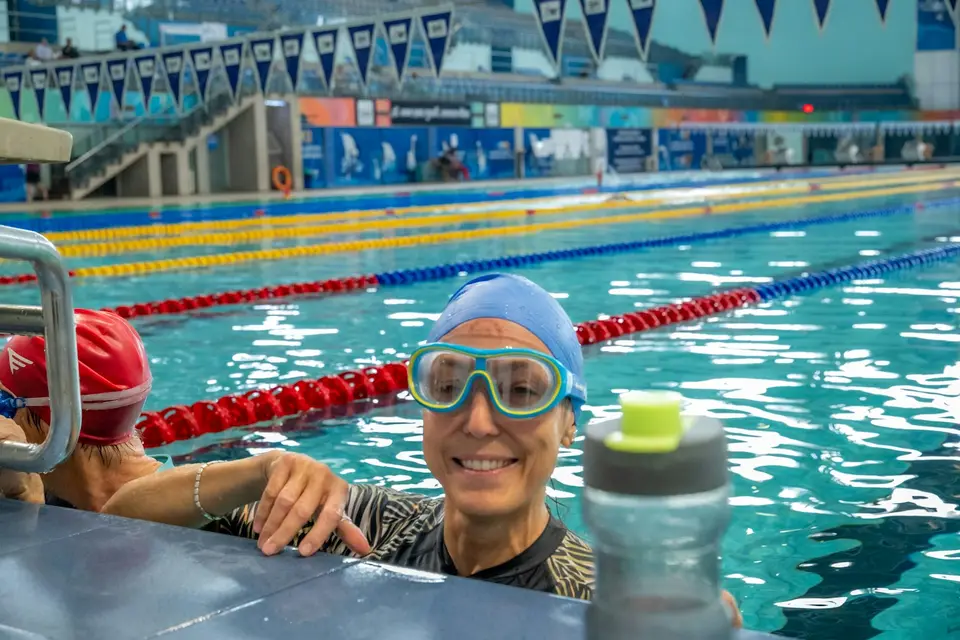Eine Schwimmerin mit Schwimmbrille lächelt am Beckenrand.