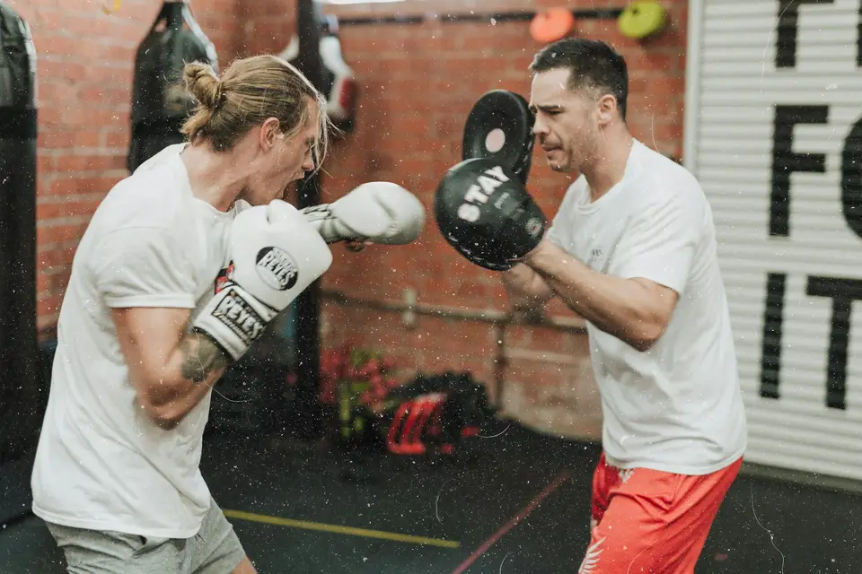 Ein Boxer schlägt beim Training auf die Pratzen seines Trainers.