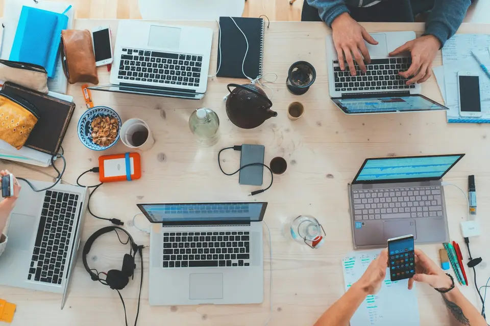 Mehrere Laptops stehen von oben gesehen auf einem Teamtisch.