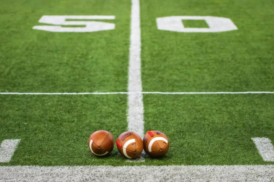 Drei Footballs liegen auf der Mittellinie eines Felds.