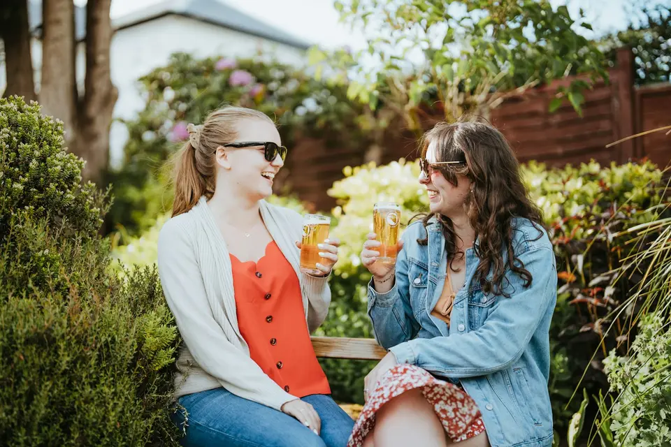 Zwei Frauen stoßen in einem Garten miteinander an.