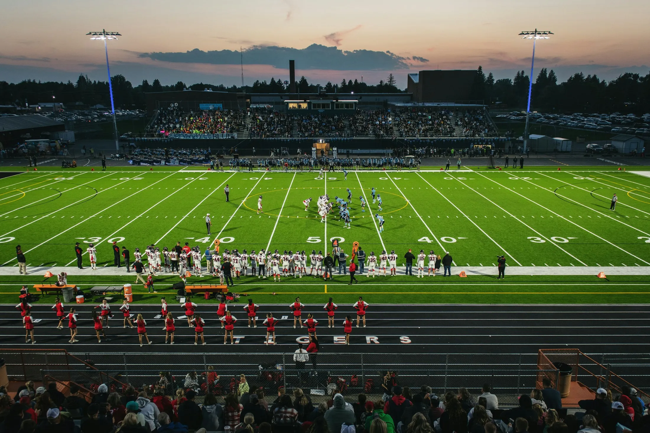 A high school football game under stadium lights at dusk.