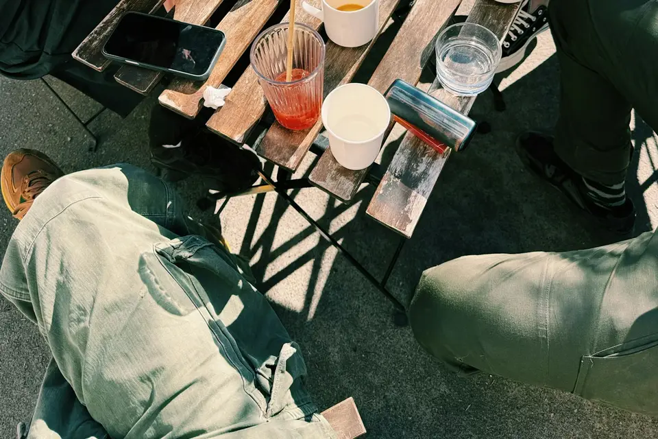 Gläser und Becher auf einem Holztisch im Freien, daneben sitzen Gäste
