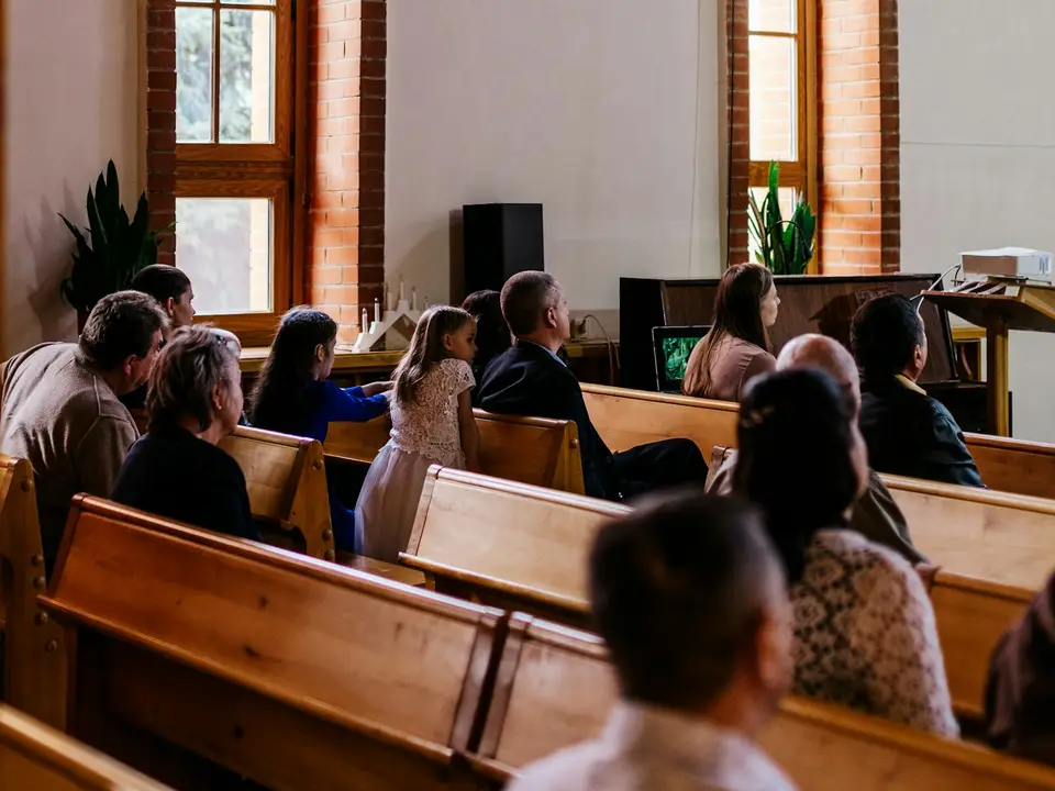A congregation gathered in a bright sanctuary with tall windows.