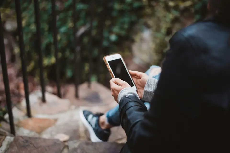 Eine Person sitzt im Freien und nutzt ihr Smartphone.