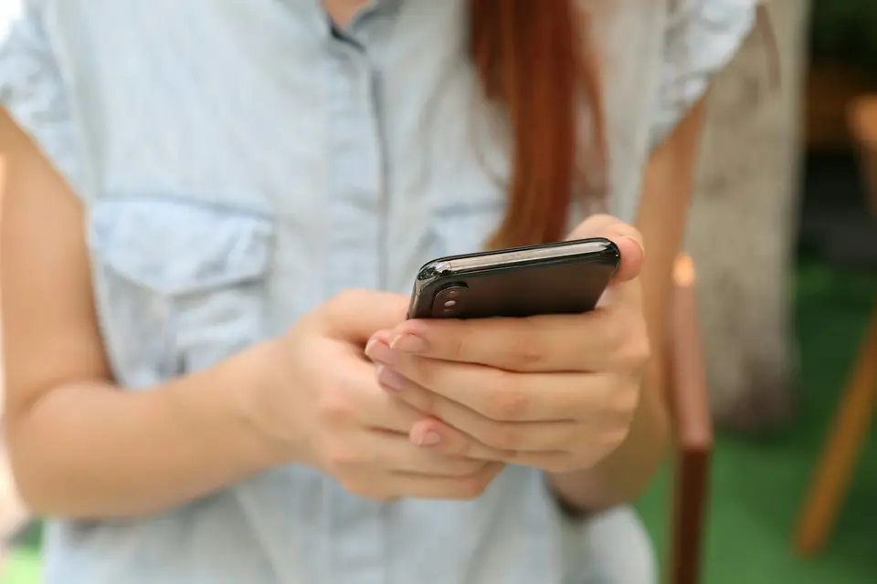 Eine Frau hält ihr Smartphone in beiden Händen.