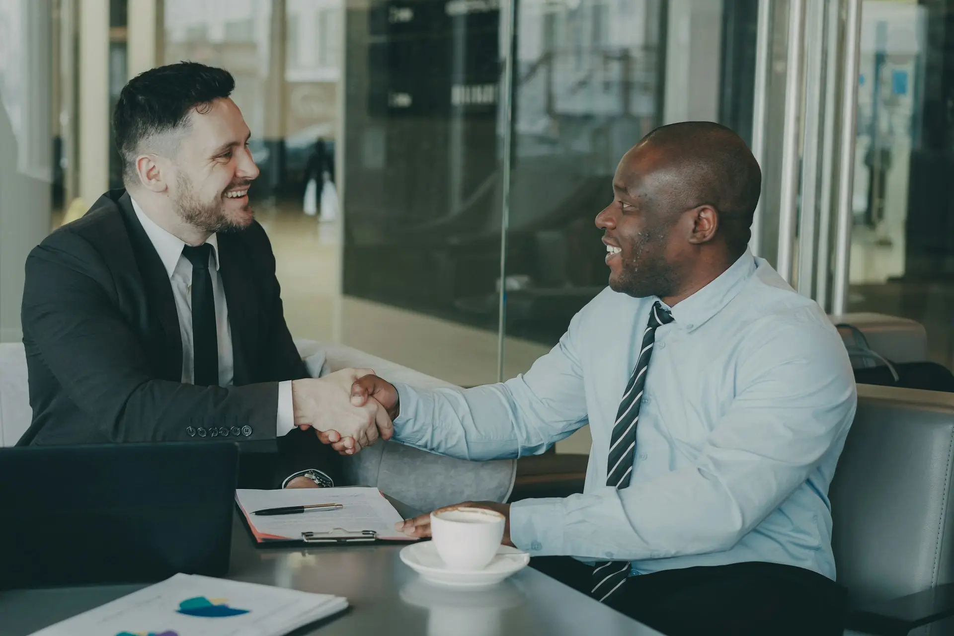Zwei Männer in Business-Kleidung geben sich nach einem Gespräch am Tisch die Hand