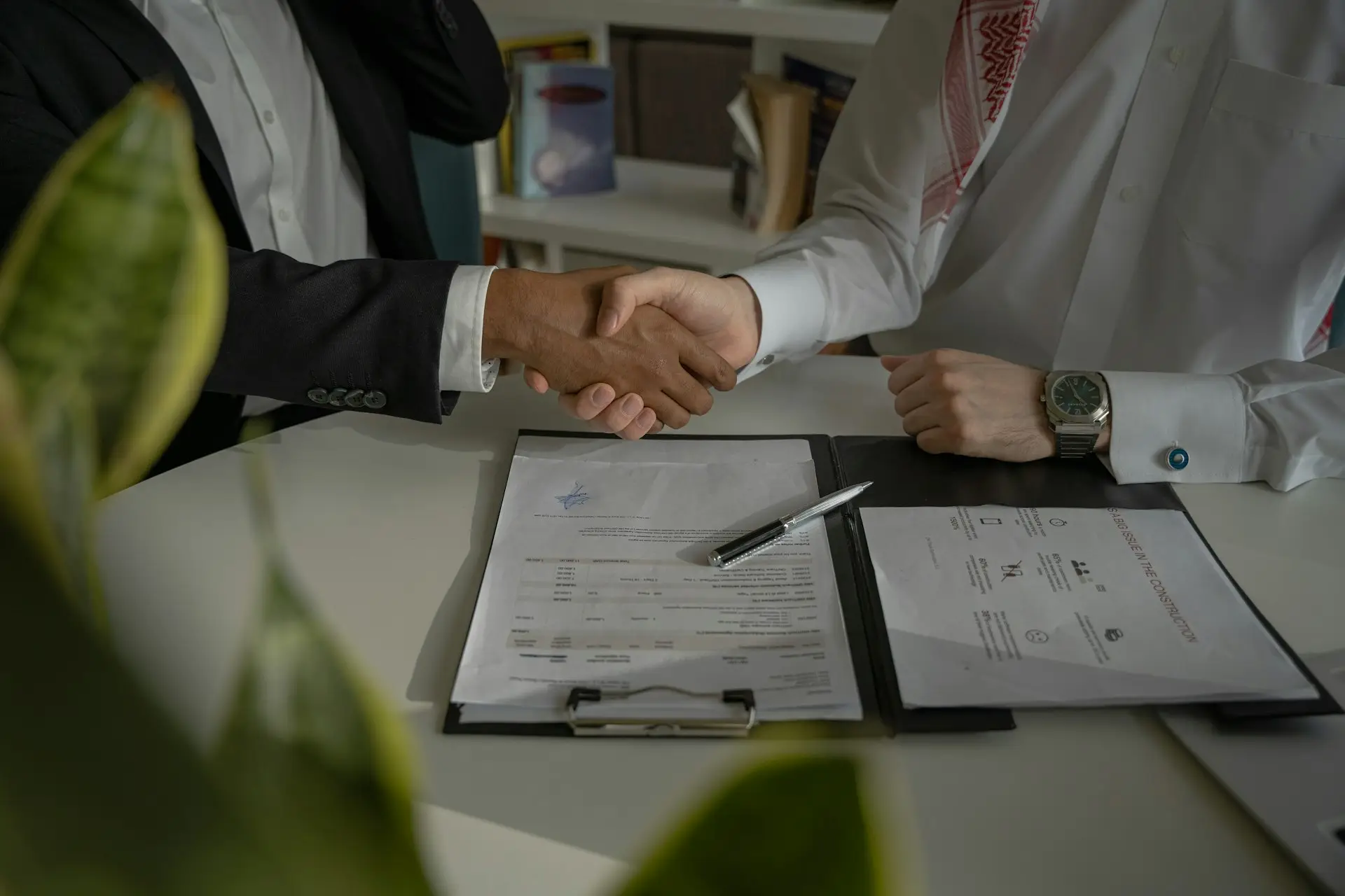 Zwei Personen geben sich über einem Tisch mit Vertragsunterlagen die Hand