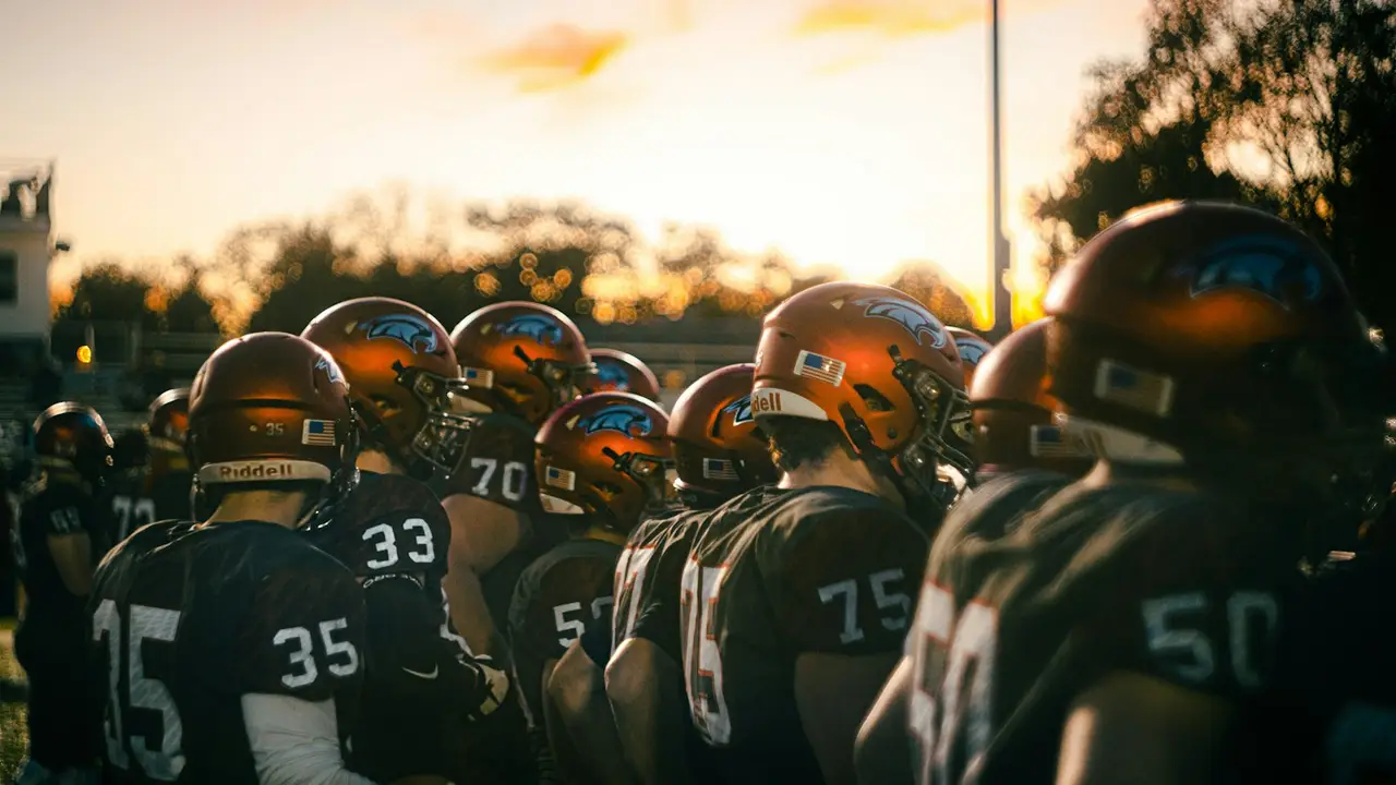 Football players in helmets lined up at sunset.