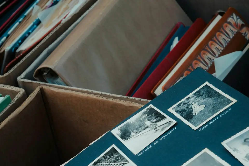 Ein altes Fotoalbum mit beschrifteten Schwarz-Weiß-Bildern liegt neben Kartons mit Büchern