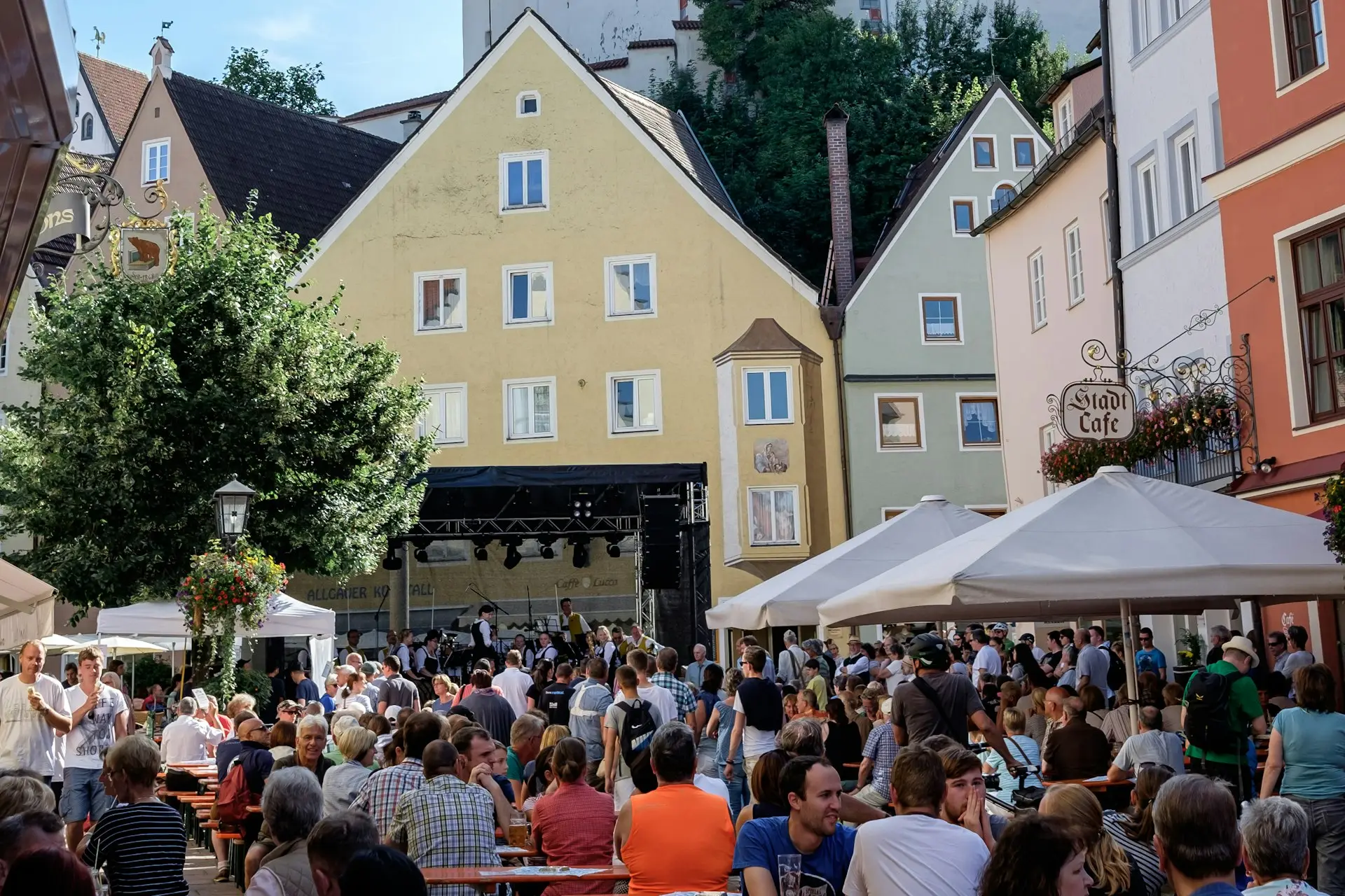 Besucherinnen und Besucher sitzen bei einem Stadtfest an Biertischen vor einer Bühne in der Altstadt