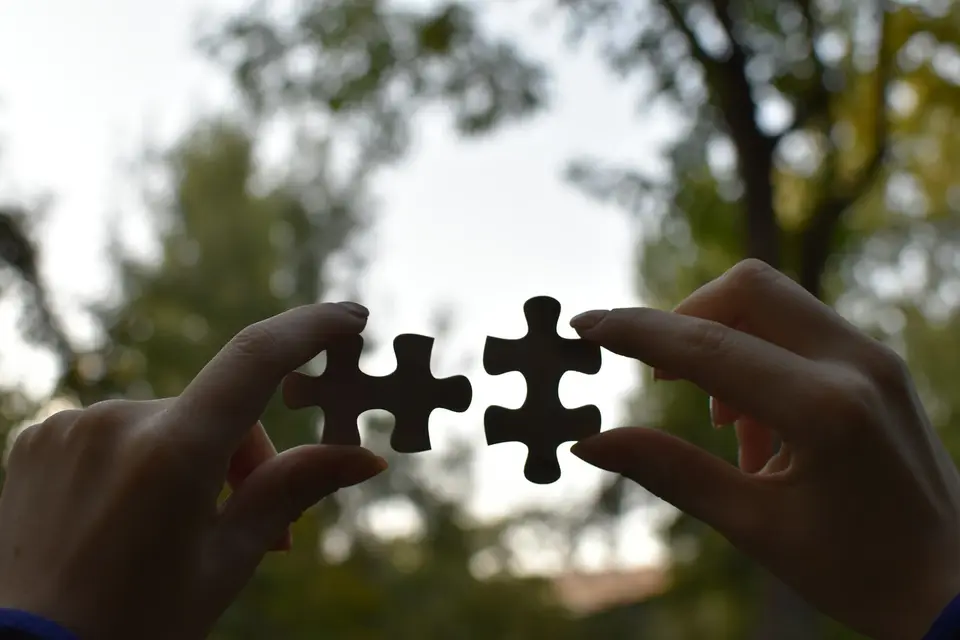 Zwei Hände halten zwei passende Puzzleteile gegen den Himmel