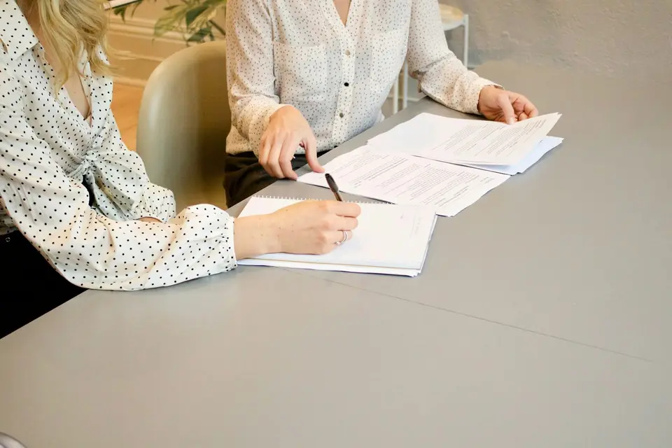 Frau unterschreibt ein Dokument, daneben eine zweite Person