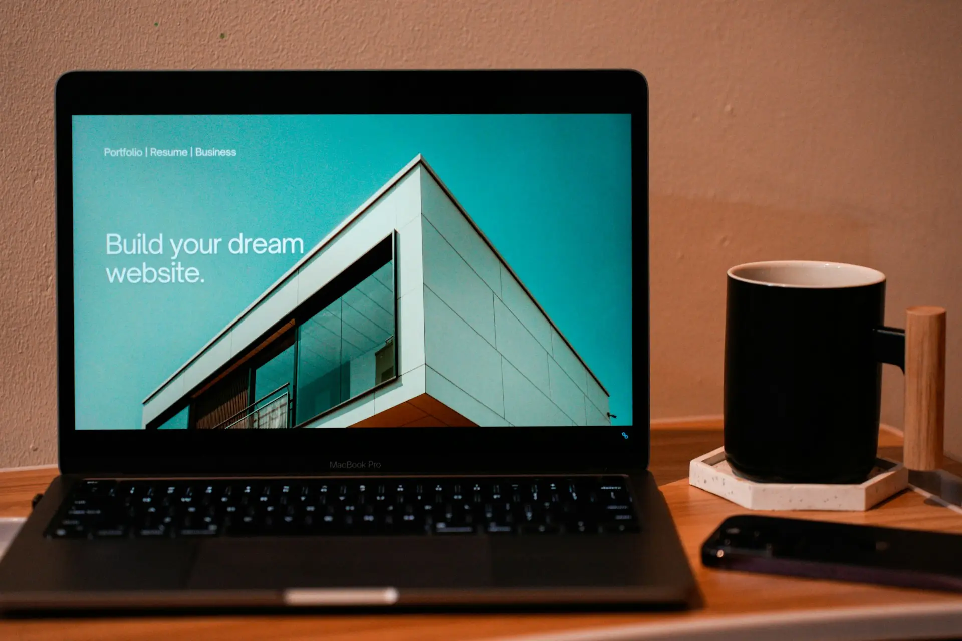 Laptop auf einem Holztisch zeigt die Startseite einer Website, daneben steht eine Tasse