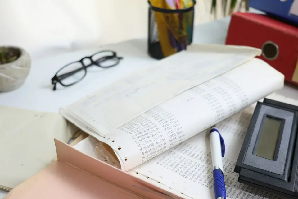 Schreibtisch mit Endlospapier-Ausdrucken, Brille, Stift und Aktenordnern