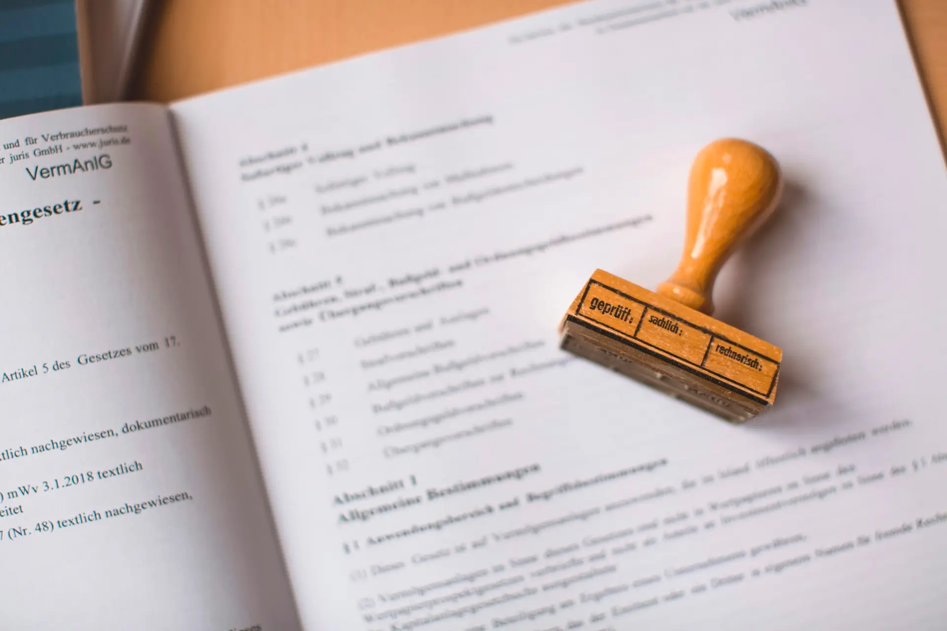 Ein Holzstempel mit der Aufschrift „geprüft“ liegt auf einem aufgeschlagenen Gesetzestext