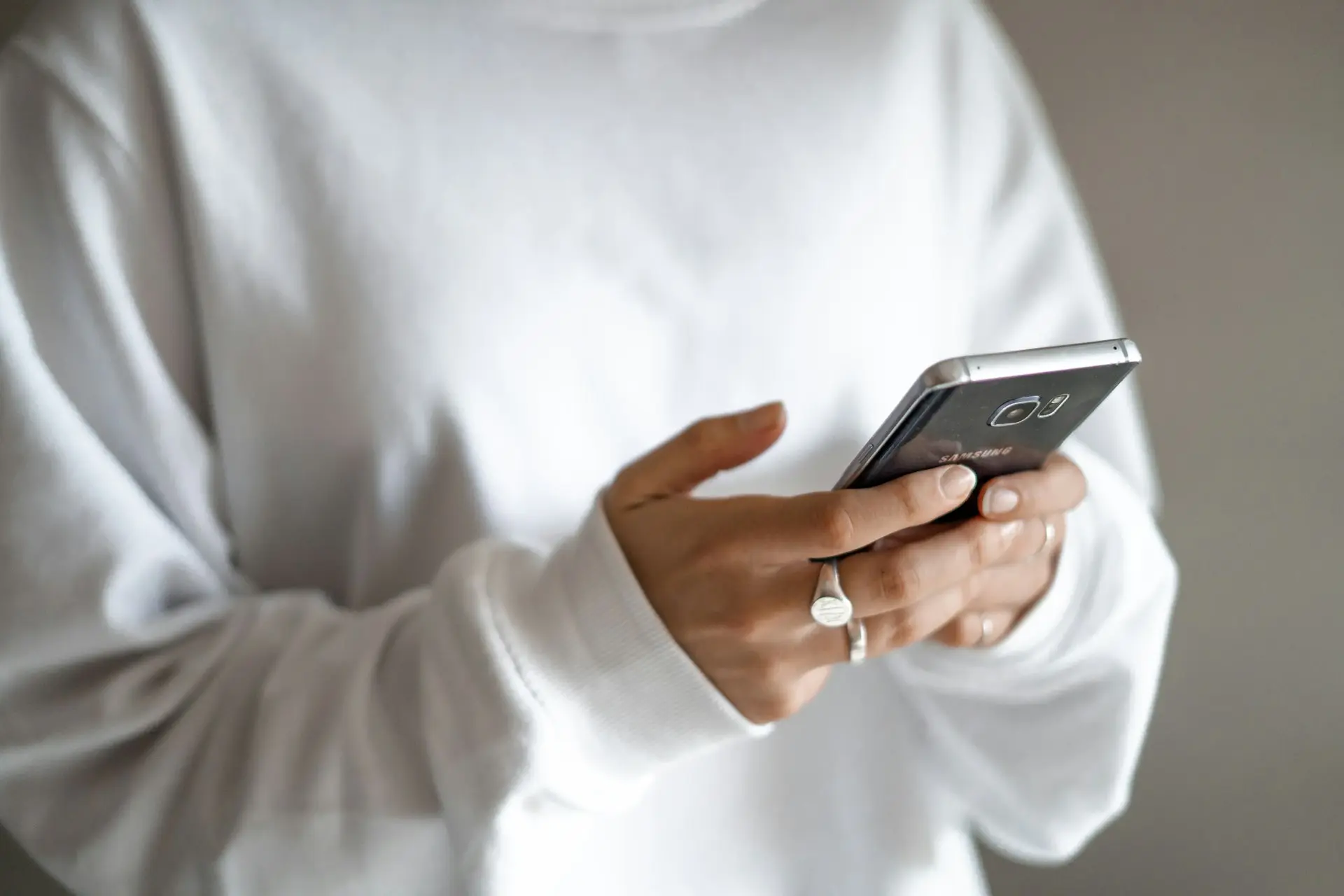 Eine Person in weißem Pullover tippt eine Nachricht auf ihrem Smartphone